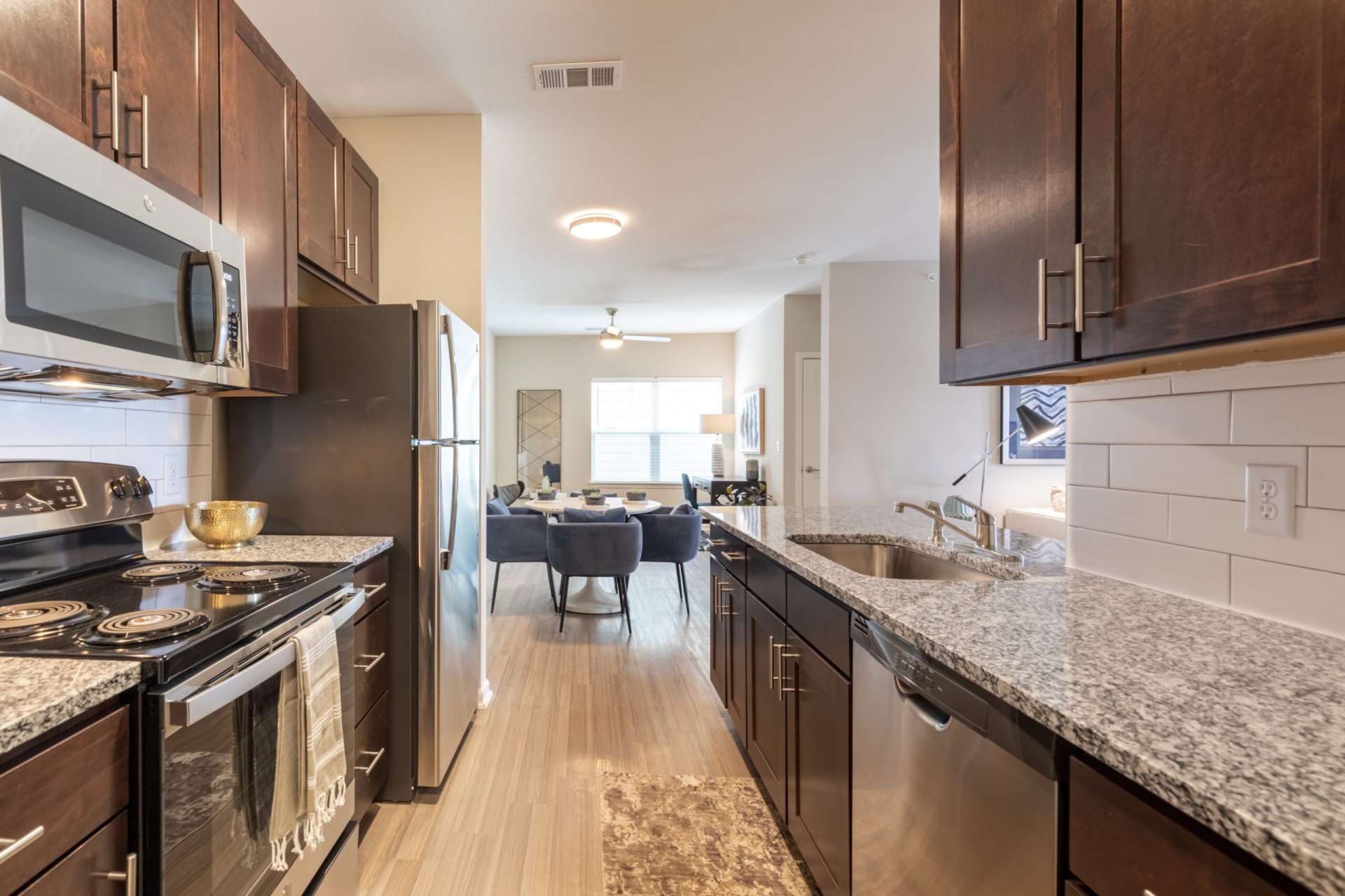 A kitchen with sink, oven, microwave, dishwasher, refrigerator, cabinets, countertops, and a view into the dining and living room spaces.